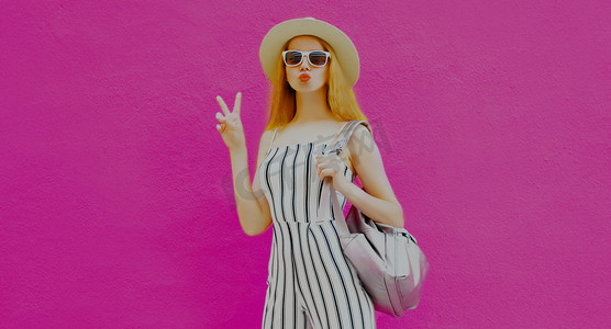 粉色甜蜜情人节摄影照片_一个时髦女人的画像，带着夏日圆圆的草帽，在五颜六色的粉色背景上飘扬着甜蜜的空气之吻