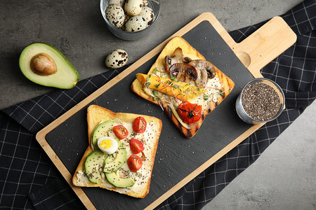 Different toasts with avocado, mushrooms, cherry tomatoes and chia seeds served on grey table, top view