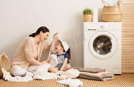 在家里洗衣服的时候，漂亮的年轻妇女和小女孩的小助手们都在开心地笑着.                               