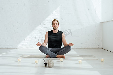 在半荷花中练习瑜伽,他在装饰着的佛头,芬芳的枝条和蜡烛旁边端坐着
