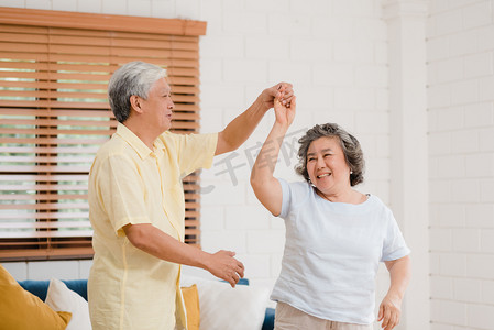 亚洲的一对老年夫妇在客厅里一边跳舞一边听音乐，甜蜜的夫妇在家里放松的时候一边享受爱情的时刻。生活方式老年人家庭在家里放松一下.