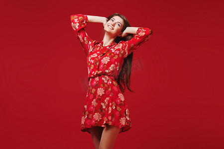 浅红底板摄影照片_一个穿着浅红色衣服，红色背景上开着花的漂亮微笑的年轻女子的画像。美丽和时尚。化妆和头发. 