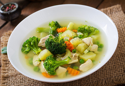 鸡汤与花椰菜, 青豆, 胡萝卜和芹菜在一个白色的碗在木制背景