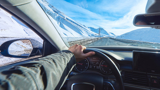 snowy mountains road view from the modern luxury car interior with drivers hand on steering wheel