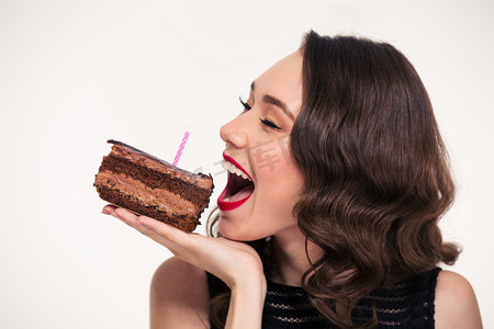 好吃极了摄影照片_Positive beautiful woman biting piece of chocolate birthday cake