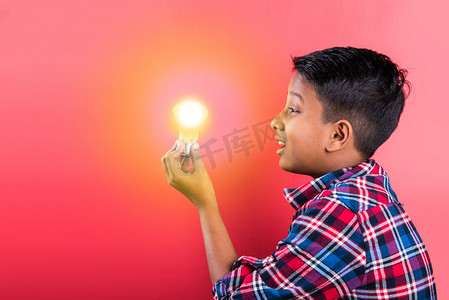 10年印度男孩拿着发光的灯泡在手，创意概念，科学概念，想法点击表达，印度男孩，亚洲男孩，红色背景，前轮廓，特写