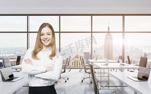 Smiling beautiful business lady with cross hands is standing in a modern panoramic office in New York City. Manhattan sunset view. Toned image.