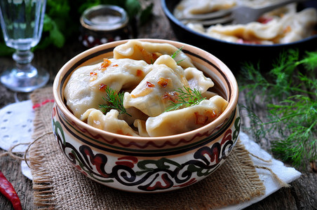 饭桌背景摄影照片_Dumplings with potatoes and mushrooms with fried onions in a traditional ceramic plate on a wooden table. Ukrainian traditional cuisine. rustic style. selective focus