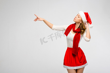圣诞圣诞老人帽子孤立的女人肖像。看起来放在一边，在灰色的背景上。穿白色和红色衣服的女孩