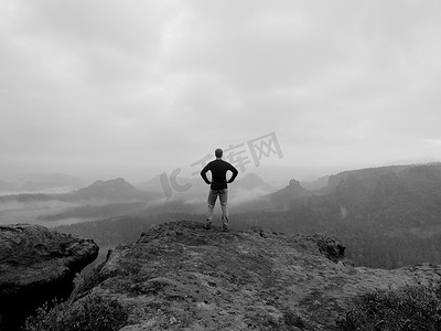 冷的男孩照片摄影照片_旅游是站在砂岩岩岩石园的高峰期，到大太阳早晨迷雾笼罩的山谷，注视。黑白照片.