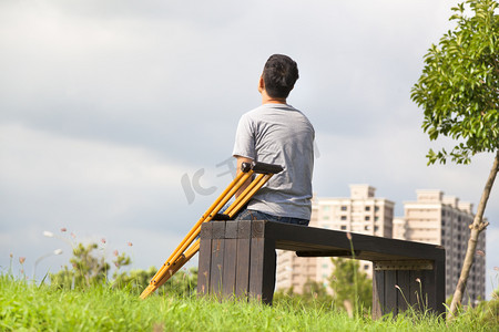 受伤的男子坐在一条长凳上的拐杖