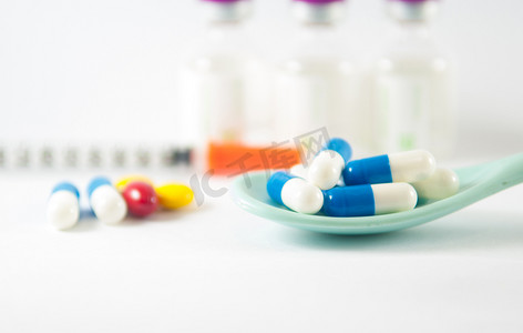 医疗药摄影照片_在医学上的汤匙里的蓝色和白色胶囊药瓶背景