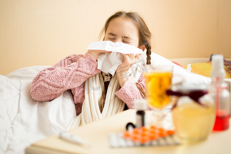 little girl lying in bed and blowing nose in paper handkerchief