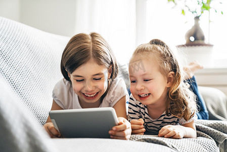可爱的小孩在玩平板电脑.快乐的女孩在家里。可爱的妹妹们在孩子们的房间里玩得很开心. 