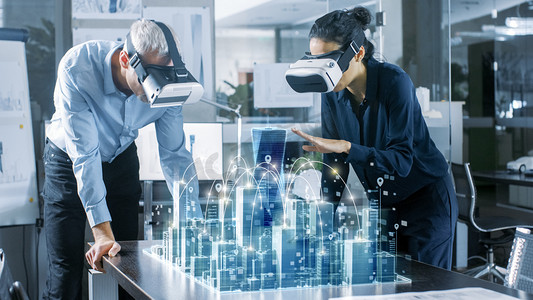 男性和女性建筑师穿着增强现实耳机工作与3d 城市模型。高科技办公专业人员使用虚拟现实建模软件应用程序.