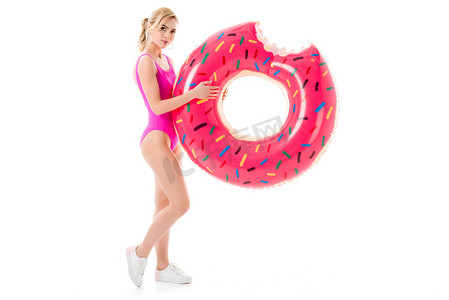 年轻女孩穿着粉红色的泳装举行甜甜圈游泳戒指在白色