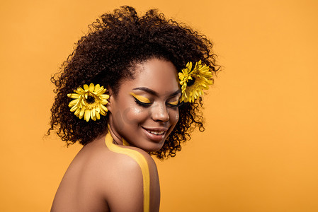年轻性感的非洲裔美国妇女与艺术化妆和 gerberas 在头发隔绝橙色背景