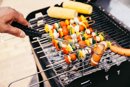 烤腊肠摄影照片_厨师检查蔬菜和香肠在户外烤烧烤