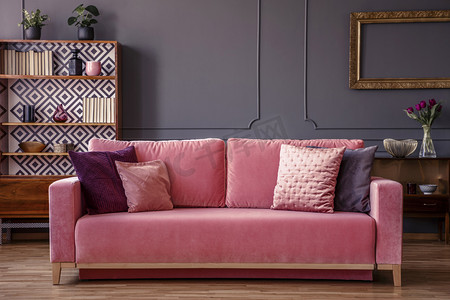 粉红色天鹅绒沙发与装饰枕头站在灰色客厅内部与老式橱柜, 新鲜的植物和墙上的造型