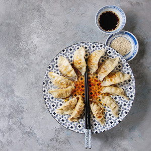 亚洲饺子 Gyozas 锅贴在白色蓝色的陶瓷盘子上, 用筷子和一碗大豆芝麻酱在灰色纹理背景上供应。顶部视图, 复制空间.