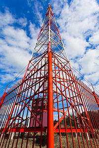 2g摄影照片_通信塔与小组天线和无线电天线和卫星盘子为移动通信 2g, 3g, 4g, 5g 以红色篱芭在塔附近反对蓝天与云彩