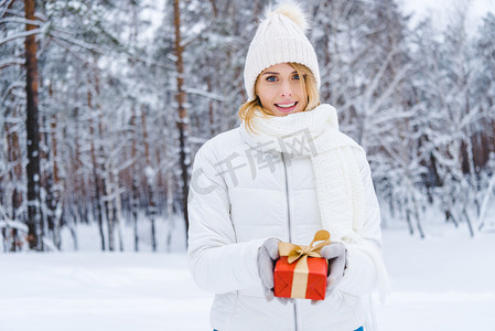 美丽的少妇藏品礼物箱子和微笑在照相机在冬天公园
