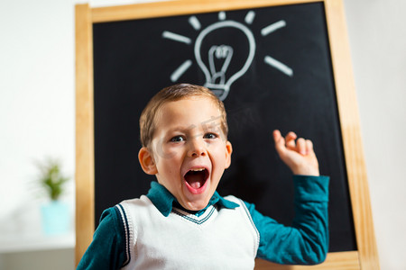 在黑板上画上电灯泡的欢呼的小男孩, 想法概念