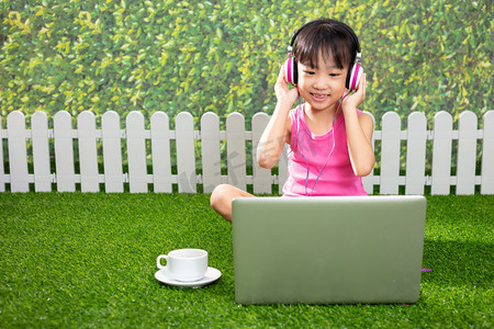 亚洲小中国女孩坐在草地上玩笔记本电脑在户外公园