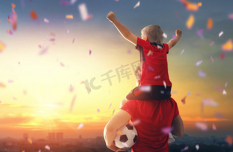 游戏游戏场景摄影照片_可爱的小孩子梦想成为一名足球运动员。男孩与人在日落踢足球。家庭体育.