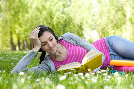女孩躺在公园的草地上与书和耳机
