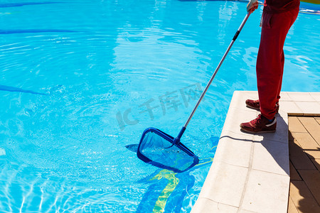 男人在夏天用刷子或站赤脚在边缘，他的下半身低视角的墙砖上蓝极网清洗游泳池.