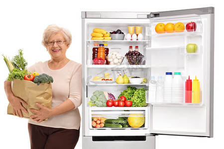 养背景摄影照片_一个成熟的女人拿着一袋杂货靠在白色背景的冰箱上