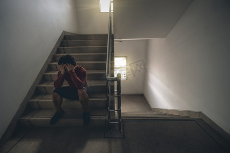 沮丧的人坐在手上楼梯在消防逃生或建筑楼梯与低光环境, 戏剧性的场景概念