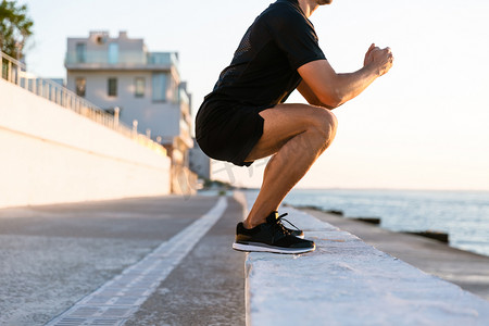 站立男人摄影照片_在海边的栏杆上的运动员站立蹲下的裁剪镜头