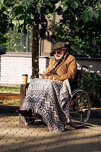 在轮椅上的高级残疾人与纸杯咖啡阅读书在街上