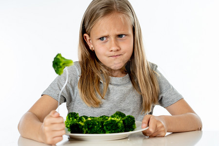 营养和健康饮食习惯为孩子健康饮食的概念。孩子们不喜欢吃蔬菜。小可爱的女孩拒绝吃健康的花椰菜在白色背景