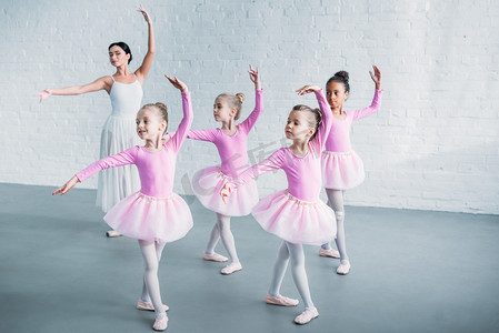 可爱的孩子在粉红色的芭蕾舞短裙裙子芭蕾学校和年轻教师一起练芭蕾