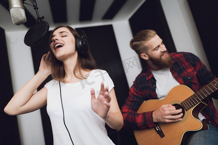一个女孩和一个男人在现代录音棚里用吉他唱一首歌。女孩唱歌, 那家伙弹吉他.