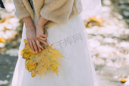 新娘穿着婚纱和天然毛皮大衣, 手捧着黄色落叶的枫树。水平