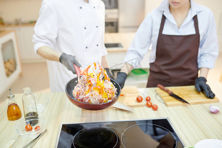 复印摄影照片_现代专业厨师的特写镜头在煎锅中混合配料, 同时在现代餐厅厨房工作, 复印空间