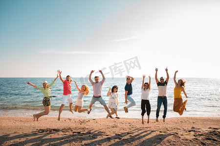 一群快乐的年轻人跳在海滩上美丽的夏日日落。九人, 五名妇女和四人。朋友和假日概念 