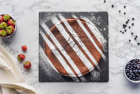 在大理石表面的石板板和新鲜浆果的美味自制棕色蛋糕的顶级视图   