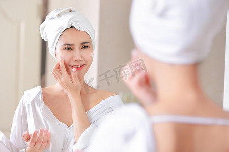 年轻的亚洲妇女在她的脸上涂抹粉底或润肤霜 