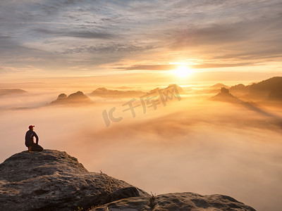 游客坐在砂岩岩石和观看到丰富多彩的雾，雾的早晨谷的高峰。可悲的男人