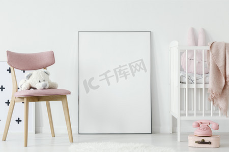 毛绒玩具在粉红色的椅子旁边的海报与样机在婴儿的房间内与床。真正的照片。粘贴您的海报在这里