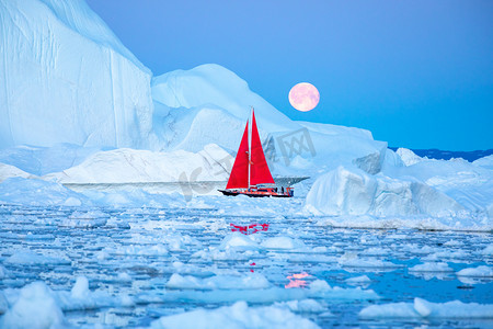 在极地夏季的午夜太阳季节, 小红帆船在迪斯科湾冰川的漂浮冰山之间游弋。伊卢利萨特, 格陵兰.