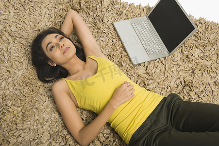 女人躺在地毯上，一台笔记本电脑
