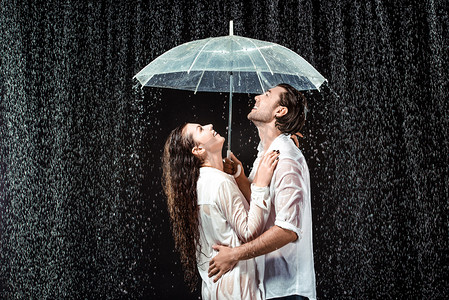 在黑色的雨滴下站在雨伞下的快乐情侣的侧面视图