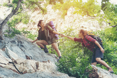 中招体育招生海报摄影照片_团体远足妇女帮助她的朋友爬上落山的最后一段。旅行团团队精神走在户外生活冒险和露营中.旅行概念.