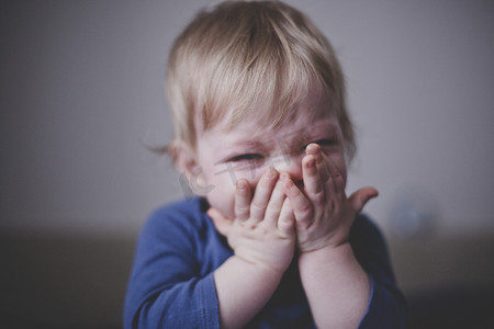 可爱的金发小宝宝穿着蓝色衣服, 痛苦地哭着, 把手压在脸上。关门了薄膜晶粒的仿化.